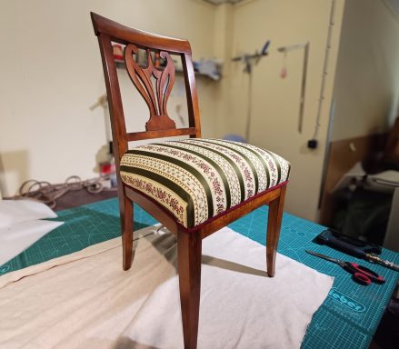 Ein Holzstuhl mit einer gepolsterten Sitzfläche und kunstvollem Rückenlehnen-Design.