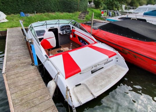 Weißes Boot mit roten Streifen, angelegt an einem Steg am Wasser.