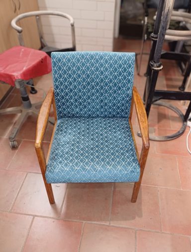 Ein blauer Stuhl mit Holzarmen und gemustertem Bezug in einem Raum.