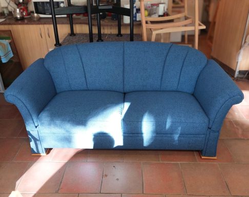 Blauer Sofa mit geschwungenen Armlehnen und gepolstertem Bezug.