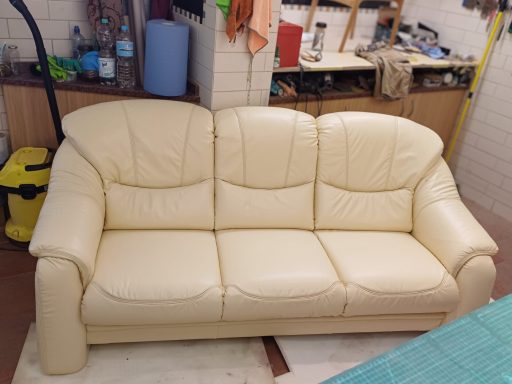 Beige Ledercouch mit drei Sitzplätzen in einem Werkstattumfeld.