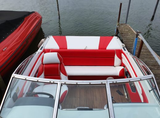Roter und weißer Bootsinnenraum mit Polsterung und Holzdeck am Ufer.