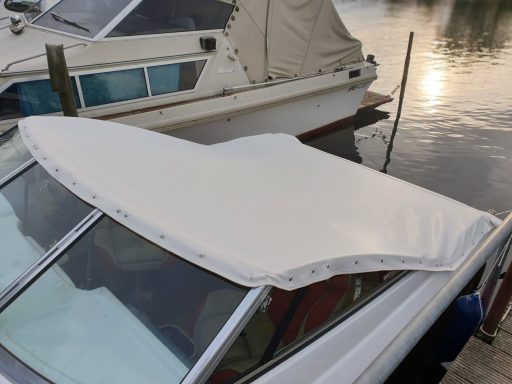 Weißes Bootspersenning auf einem Boot, am Ufer eines ruhigen Gewässers.