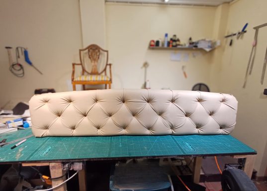 Beige gepolsterte Rückenlehne mit Knöpfen auf einem Tisch in einem Werkstattumfeld.