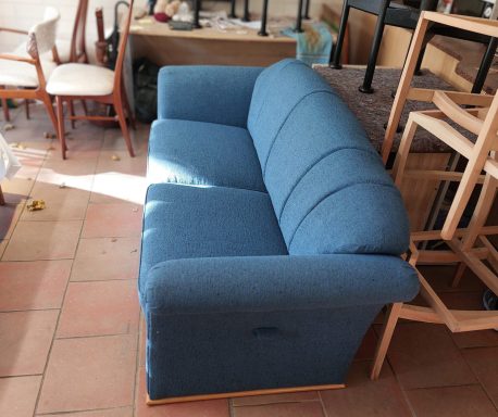 Blaues Sofa mit geneigten Armlehnen auf einem gefliesten Boden.