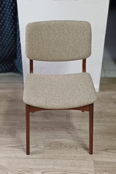 Beige gepolsterter Stuhl mit Holzbeinen vor einer hellen Wand.